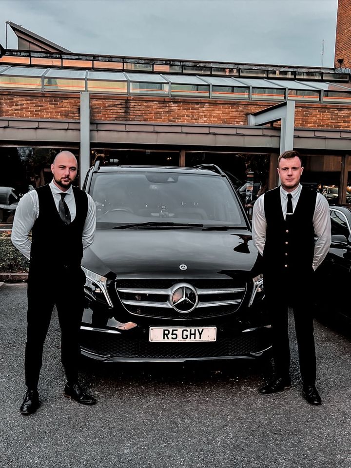 Two R5 chauffeurs in black waistcoats and ties, standing either side of the V-Class