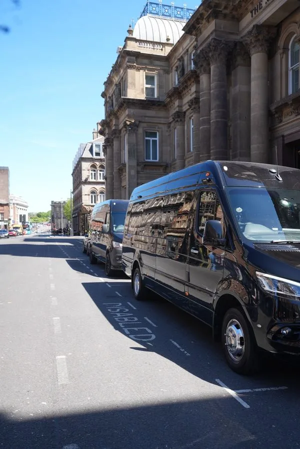 A black R5 Mercedes Sprinter parked outside a domed sandstone building in the city centre, with more Sprinters behind